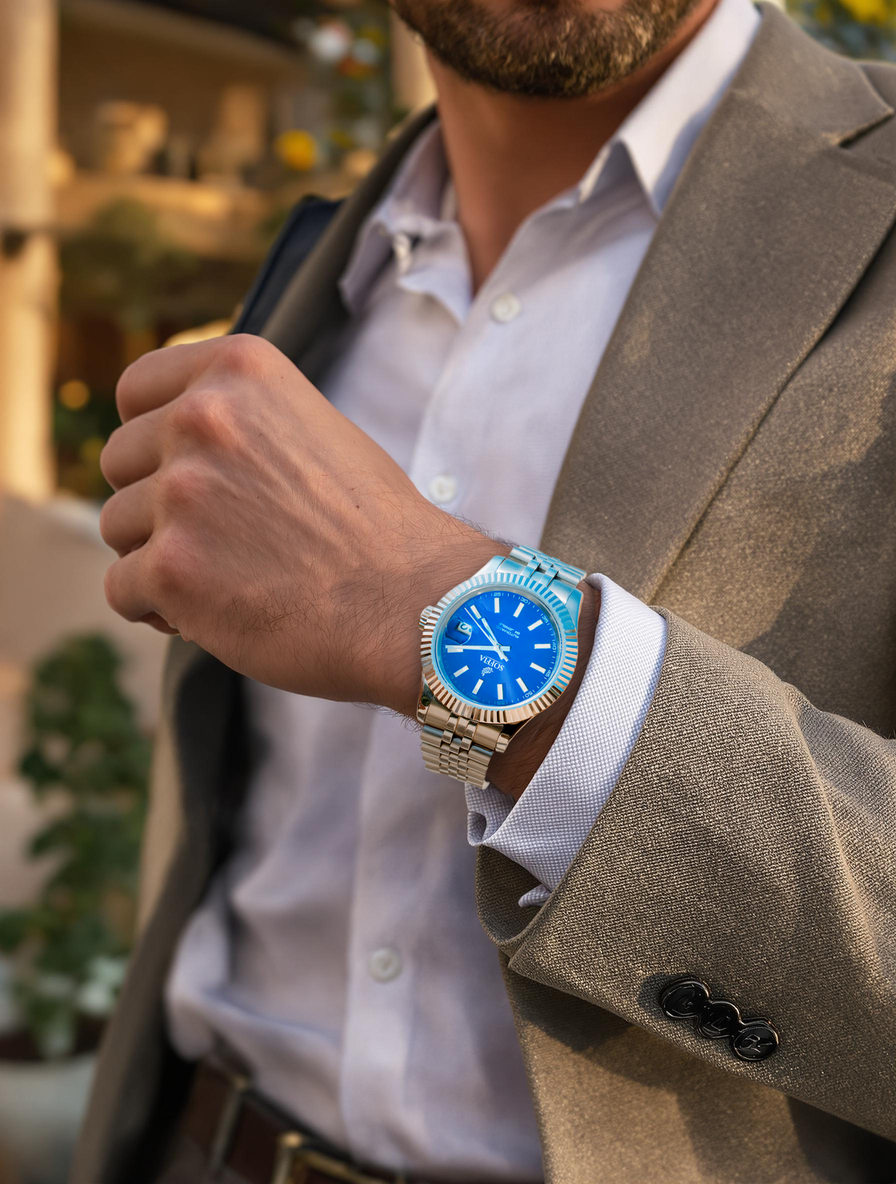 A person wearing a suit has their arm raised to show a deep navy blue dial watch with a polished stainless steel case.