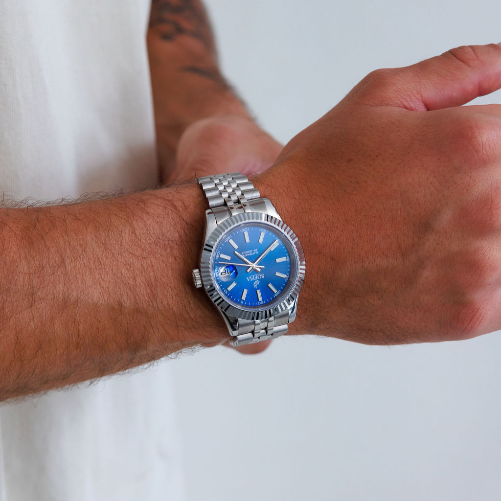 Hand wearing a silver watch with a blue face on a white background