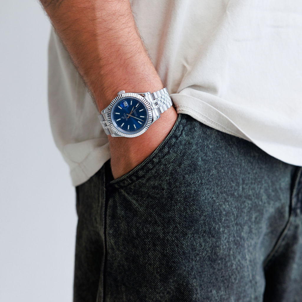 Person wearing a silver watch with a blue face on a plain background