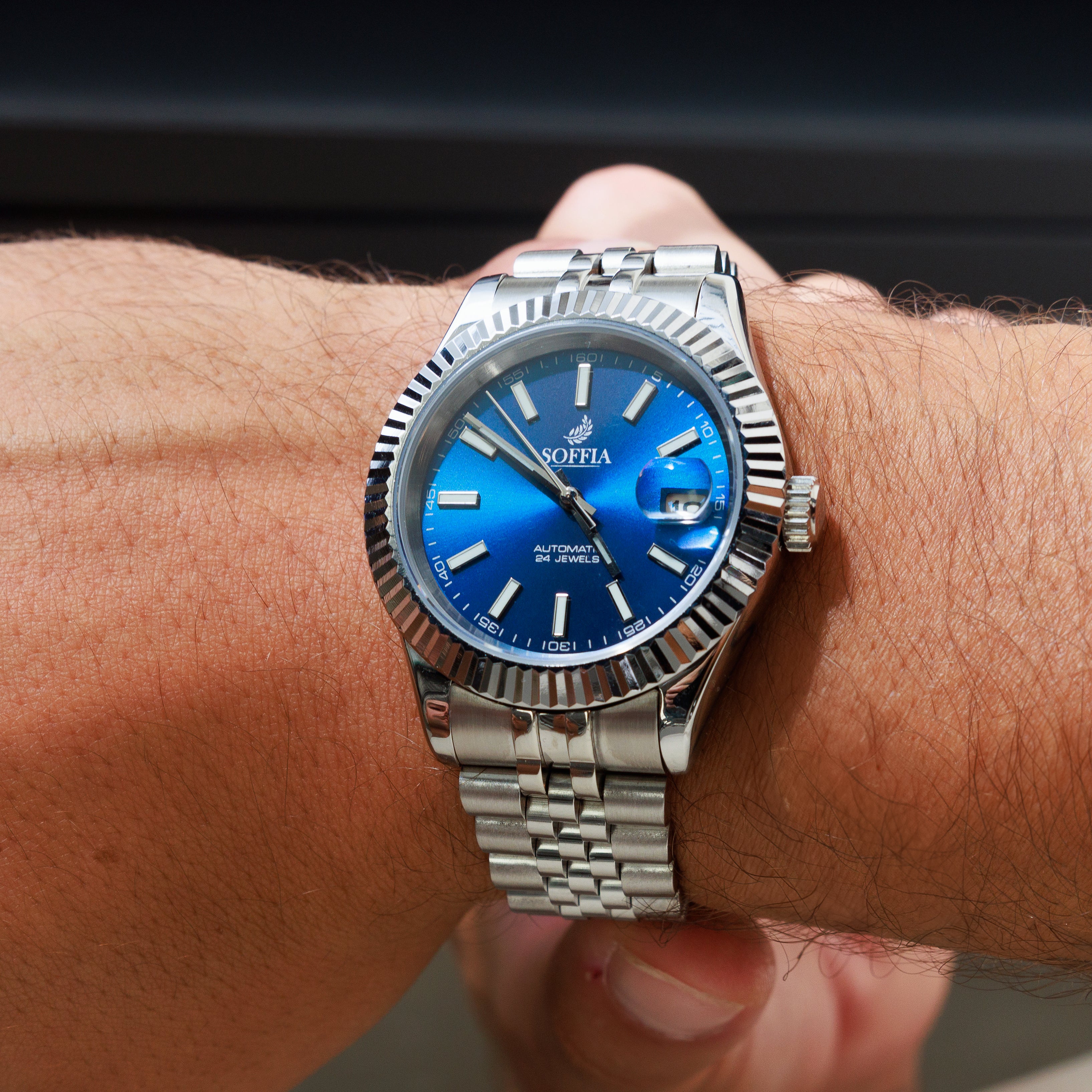 Silver watch with a blue face on a wrist against a blurred background