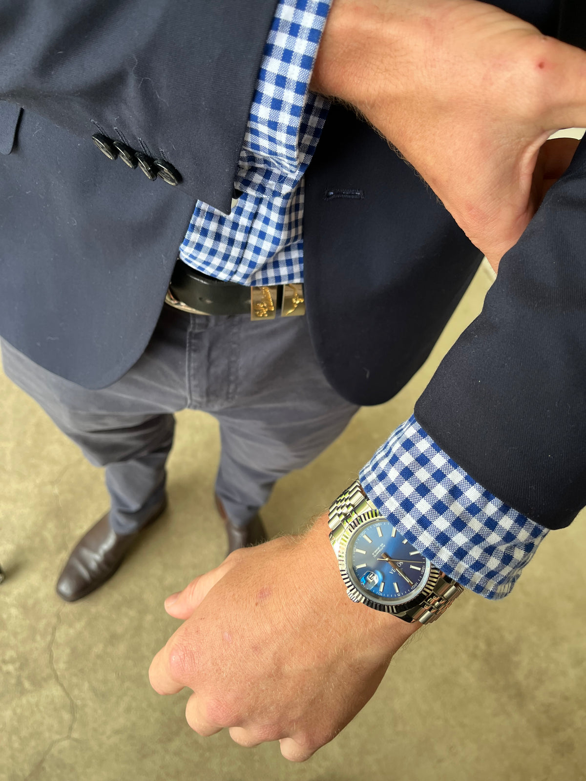 Person wearing a blue checkered shirt with rolled-up sleeves, a watch, and a belt.