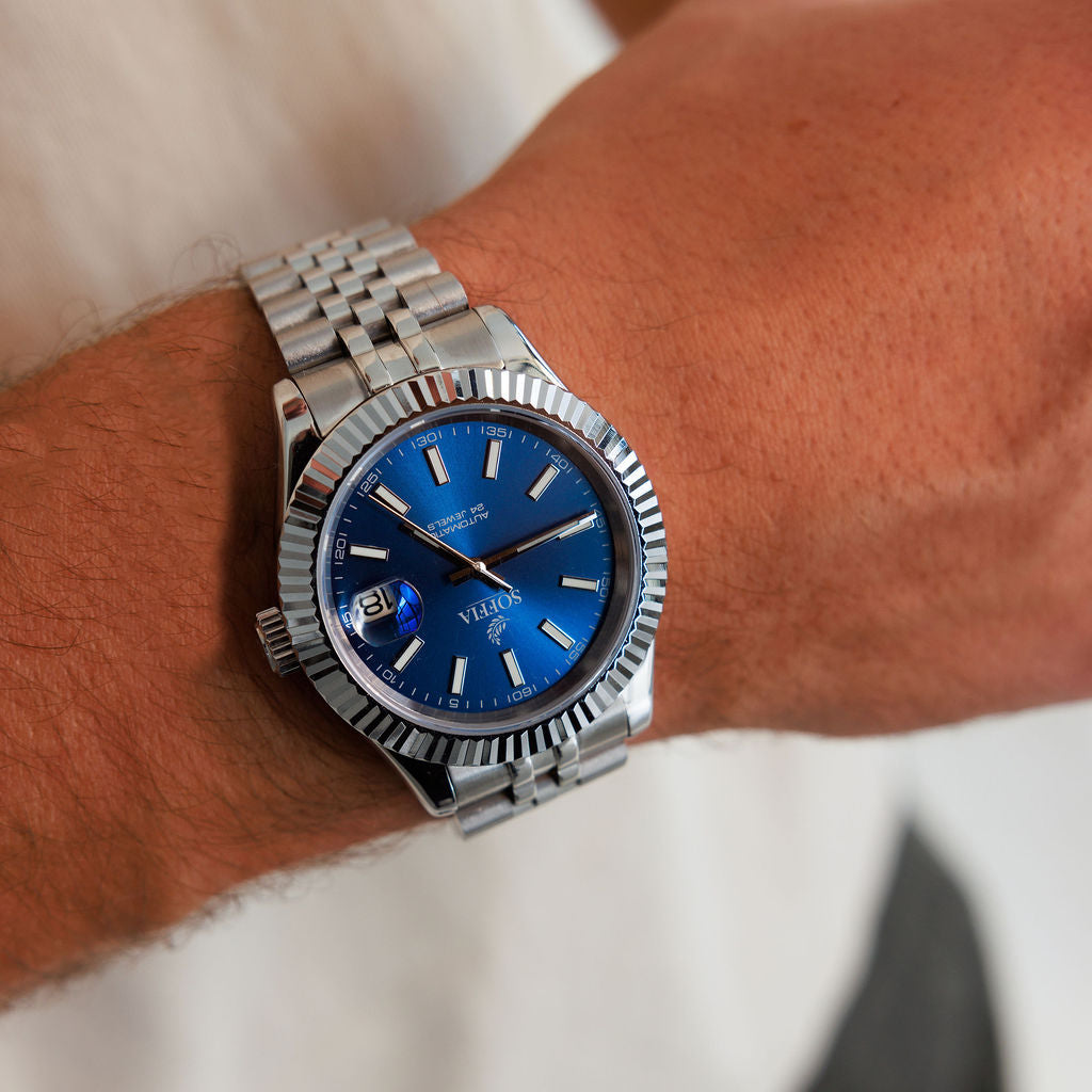 Silver watch with a blue face on a wrist against a neutral background
