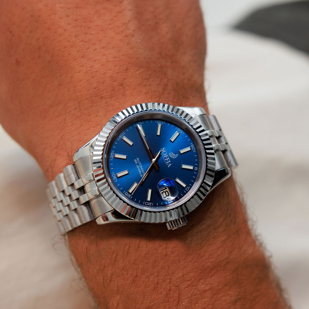 Silver watch with a blue face on a wrist against a neutral background