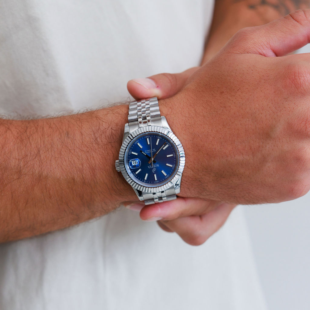 Close-up of a wrist wearing a silver watch with a blue face on a white background