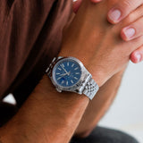 Silver watch with a blue face on a wrist, held by another hand.
