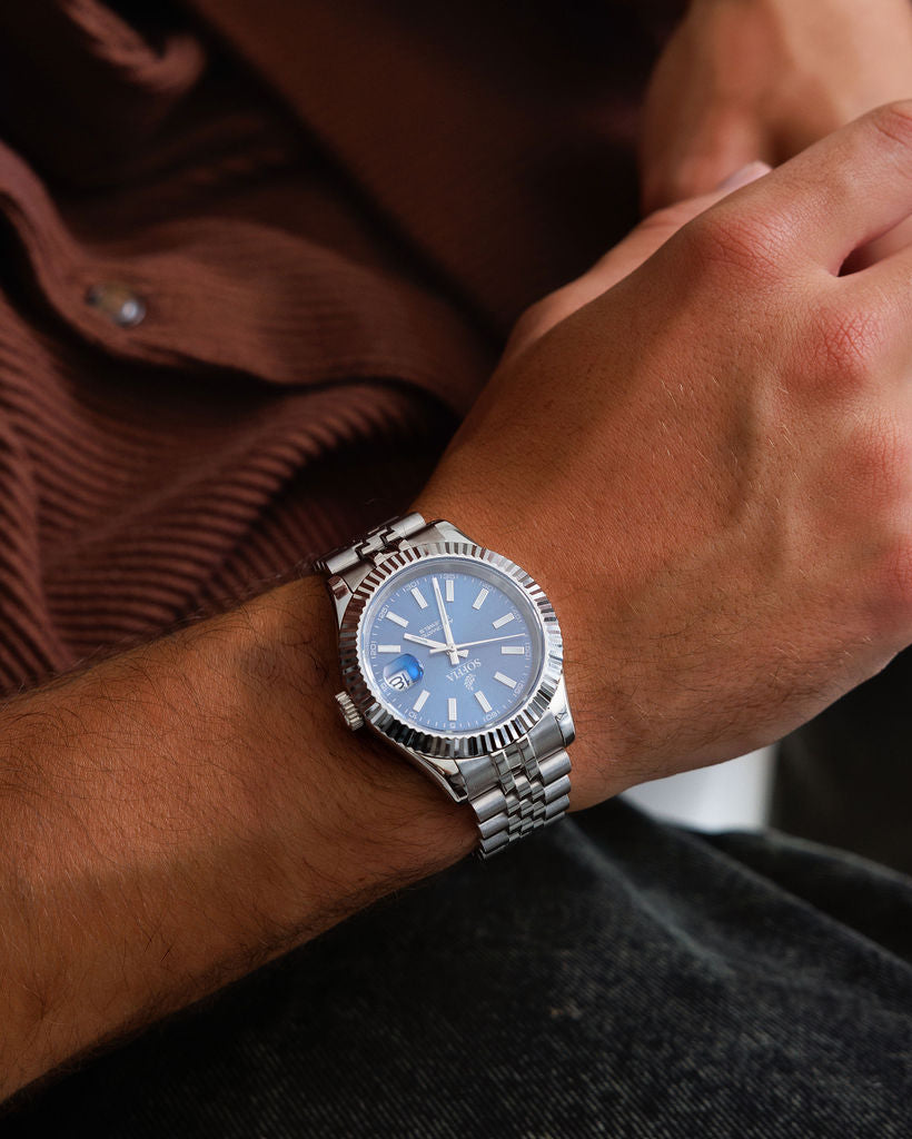 Close-up of a wrist wearing a silver watch with a blue face.