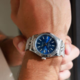 Silver watch with a blue face on a wrist against a neutral background