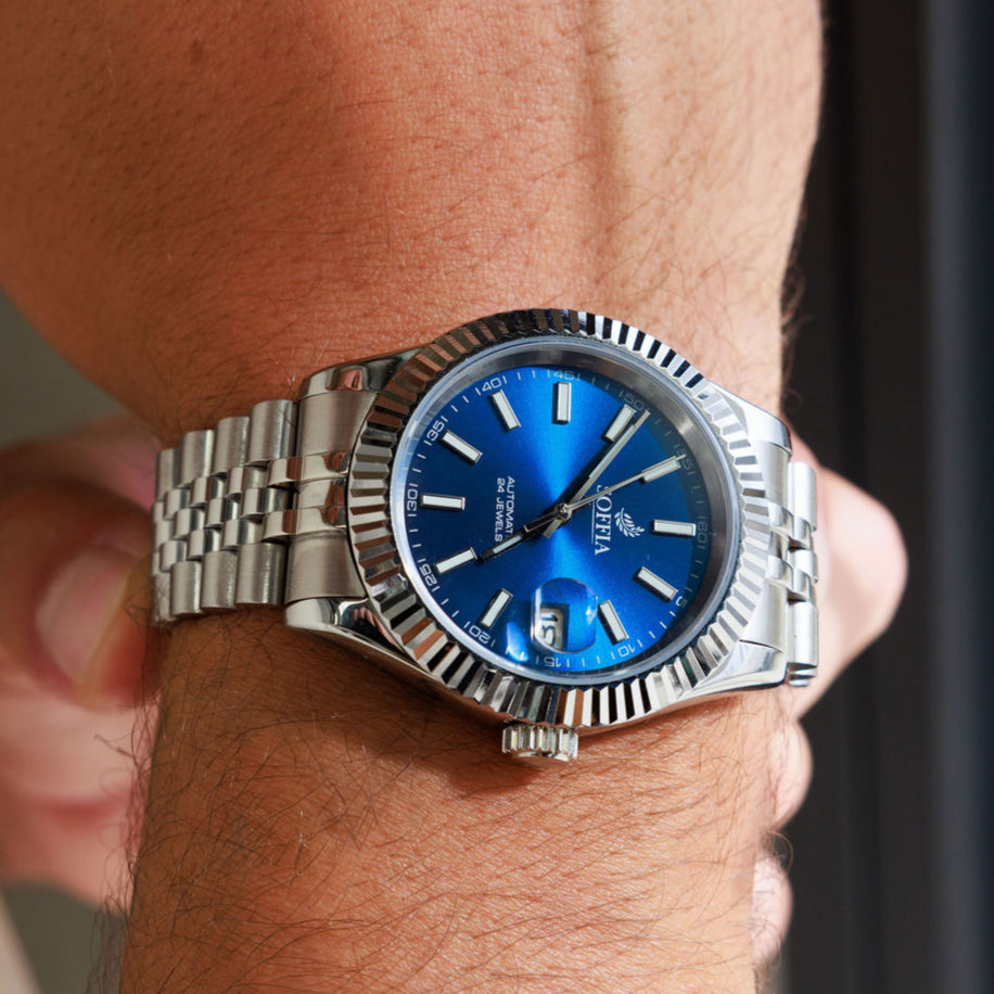 Silver watch with a blue face on a wrist against a neutral background