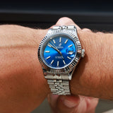 Silver watch with a blue face on a wrist against a dark background